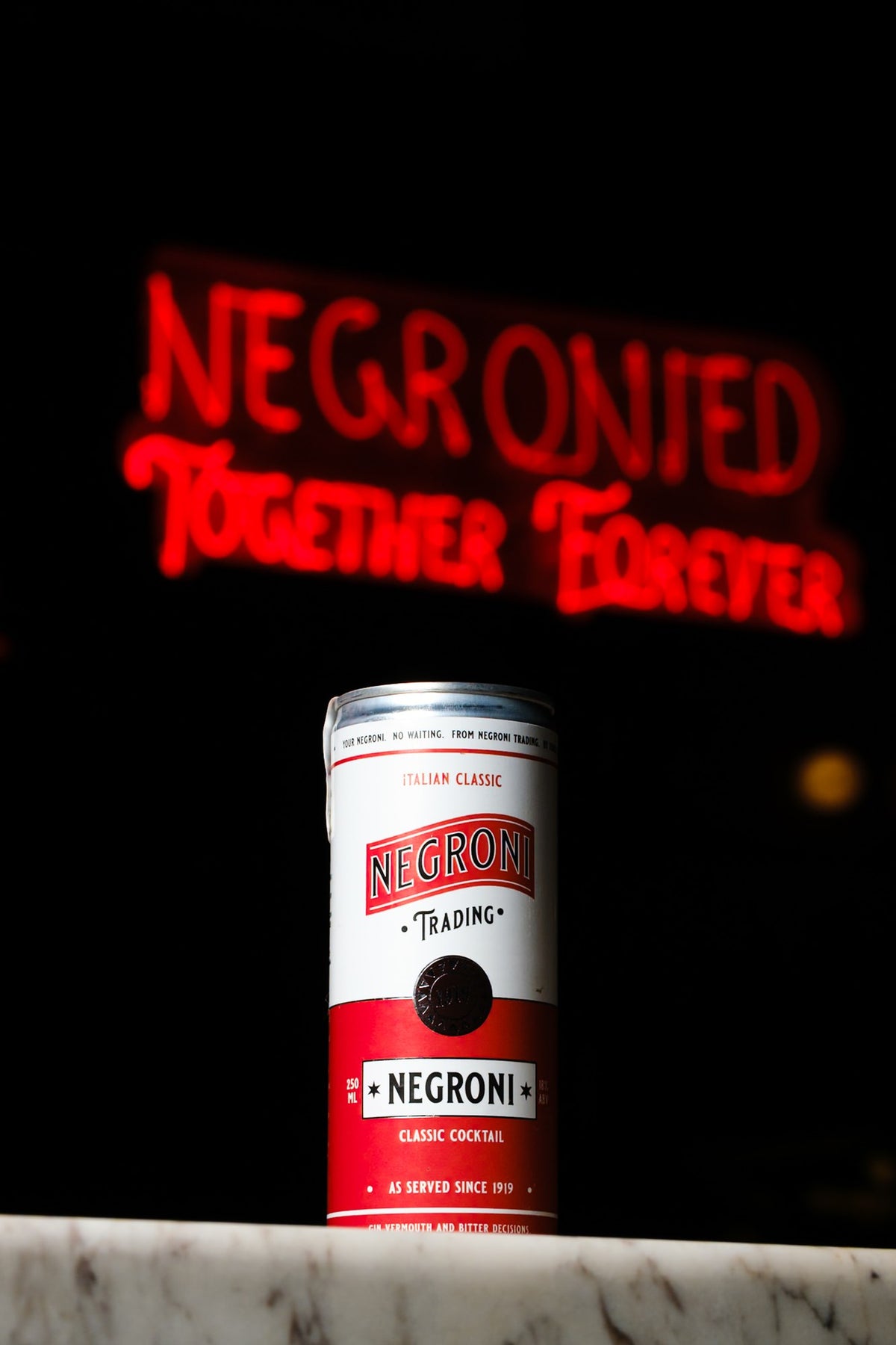 Negroni Cocktail Original can on a marble bar, with a red neon sign in the background